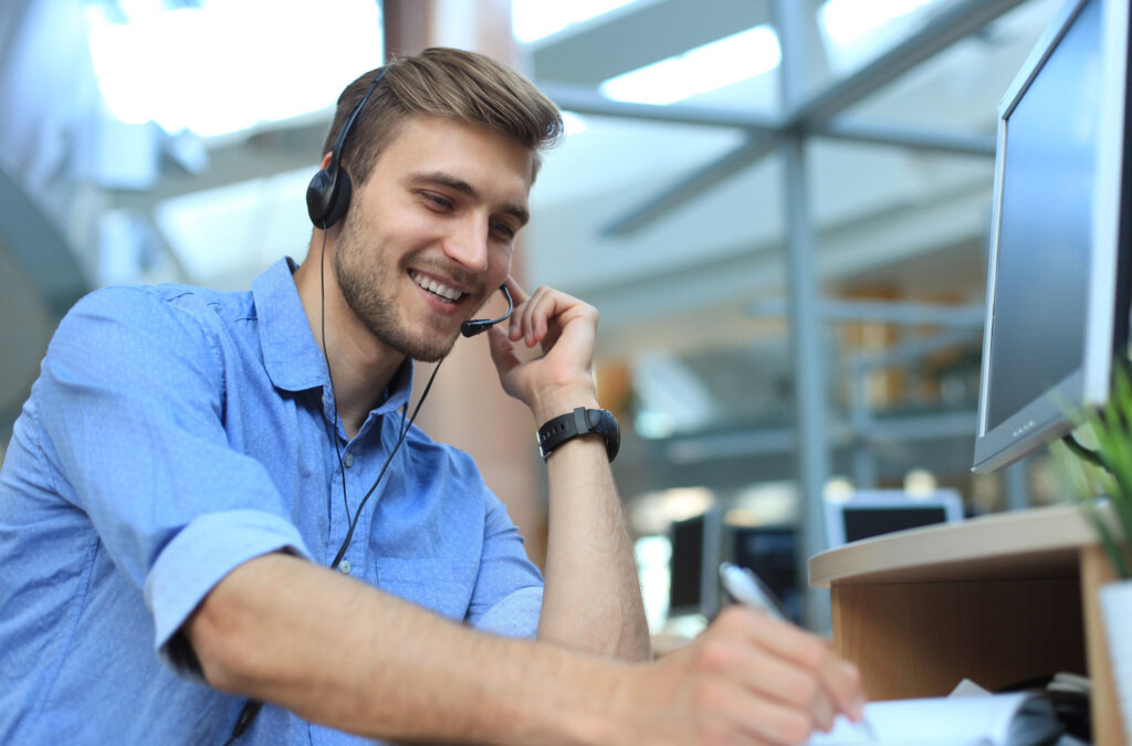 Tipps für den E-Commerce. Das Bild zeigt einen Mann mit Headset, der an einem Schreibtisch sitzt. Er lächelt, während er einen Anruf bearbeitet.